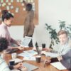 Group of people working with wooden table, paper charts, laptops, and digital tablet in bright office