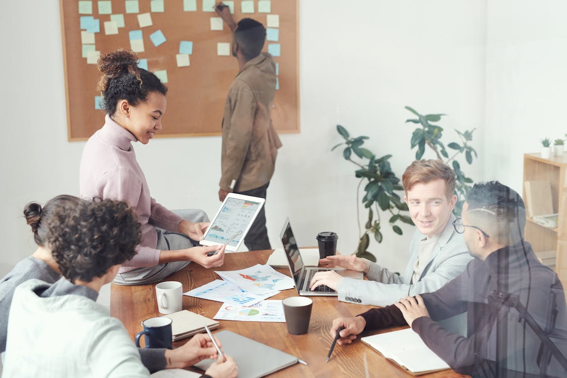 Group of people working with wooden table, paper charts, laptops, and digital tablet in bright office