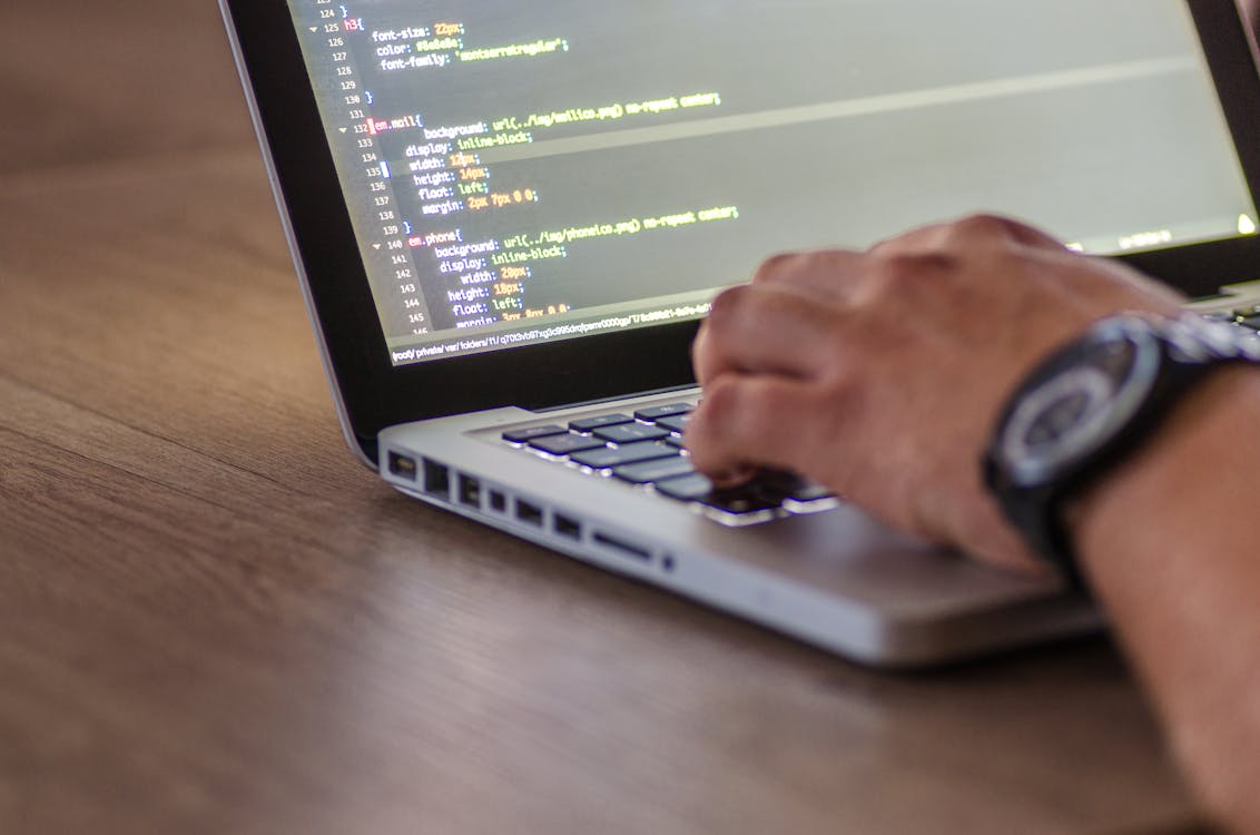 Person typing code on a silver metal laptop keyboard on a wooden desk