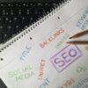 spiral notebook with SEO keywords handwritten in colored pencil on graph paper over black laptop keyboard