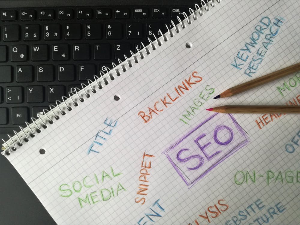 spiral notebook with SEO keywords handwritten in colored pencil on graph paper over black laptop keyboard