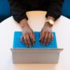 Person typing on blue plastic keyboard attached to silver laptop on white round table