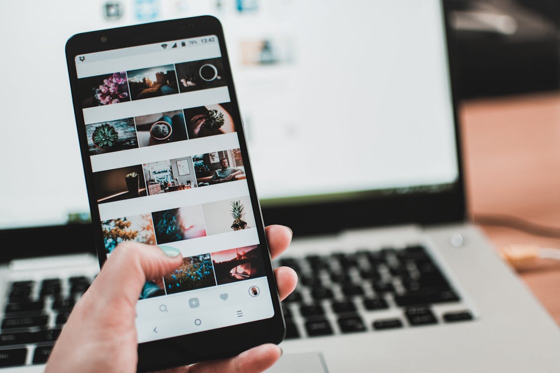 Hand holding black smartphone with photo gallery app open, in front of silver laptop keyboard