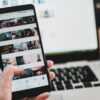 smartphone displaying photo gallery app held in hand with metal laptop keyboard in background