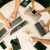 Round table with silver laptops, black smartphones, glass cups, and notebooks on white tiled surface