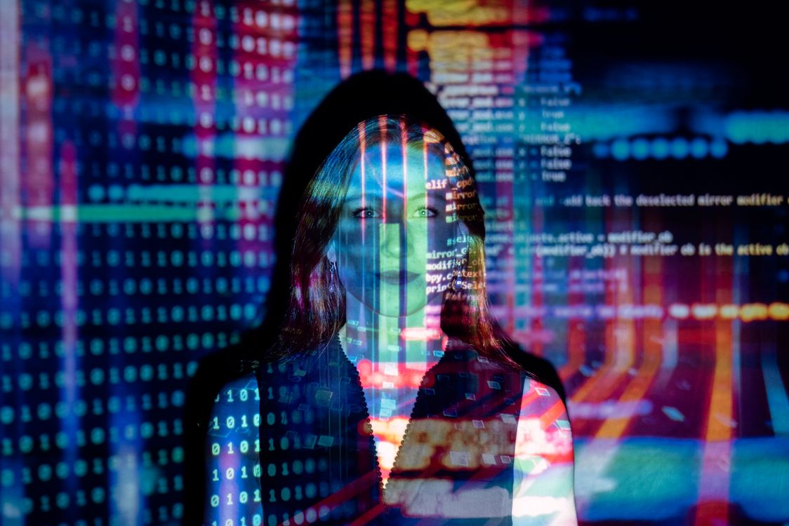 Woman with digital code and data projections on her face and clothing in multicolored light
