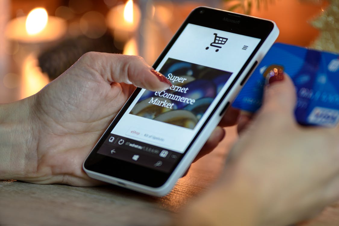 Smartphone with white plastic case displaying e-commerce site, held by hands with a blue credit card
