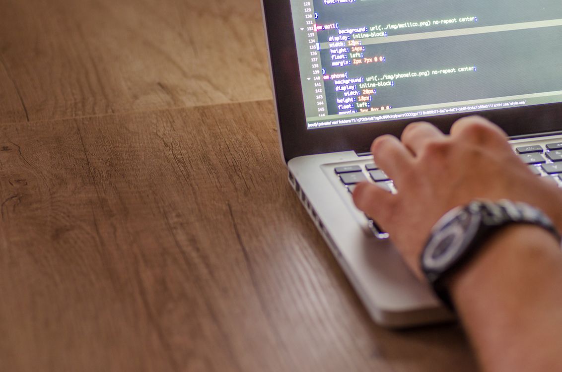laptop with metal casing displaying code on screen with hand typing on wooden surface