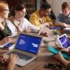 Group of people using laptops and tablets on a wooden table with small potted plants