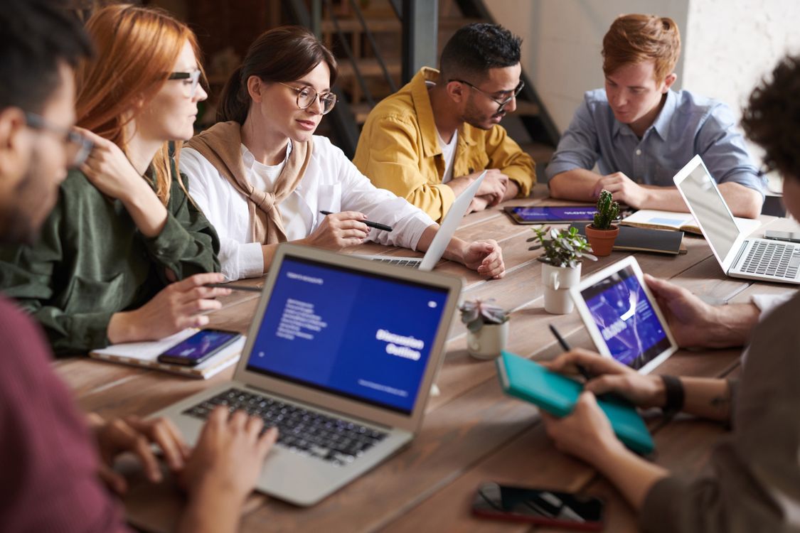 Group of people using laptops and tablets on a wooden table with small potted plants