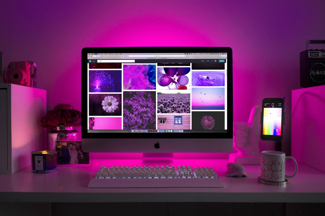 desktop computer with metal frame and screen displaying purple images on white desk with white keyboard and pink lighting