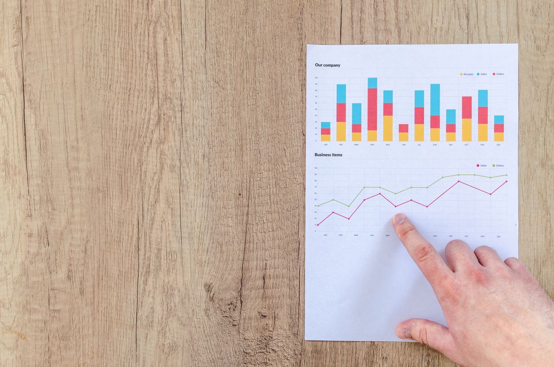 Hand pointing at printed paper with colorful business charts on wooden surface