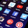 smartphone screen displaying colorful social media app icons on glass surface