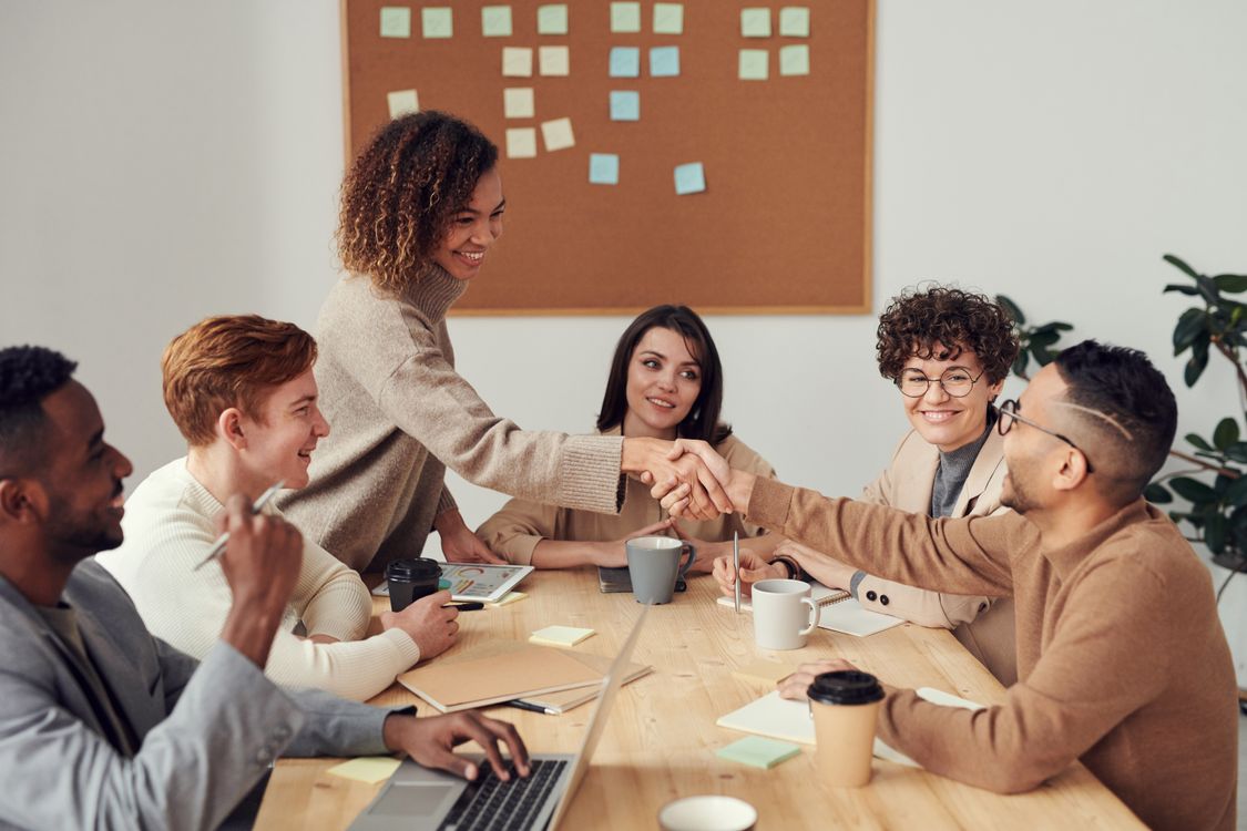 People shaking hands over a wooden table with coffee cups and laptops in a meeting room