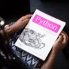 Person holding a white paper book titled Python with a snake illustration and pink text