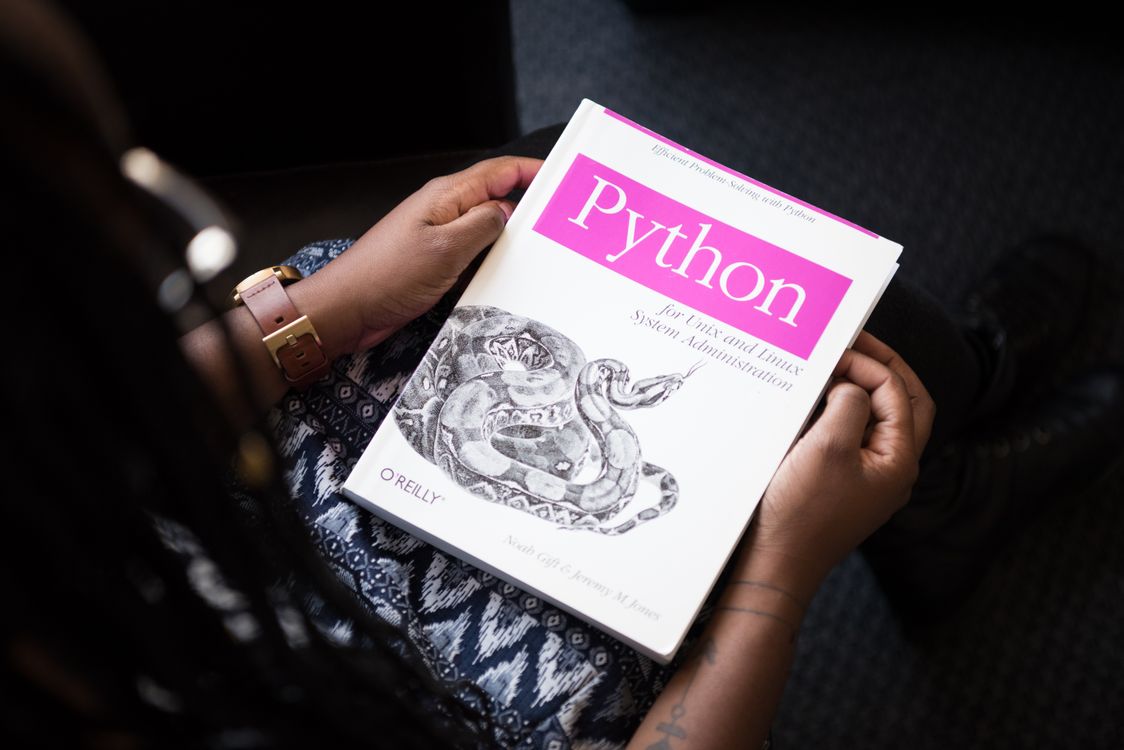 Person holding a white paper book titled Python with a snake illustration and pink text