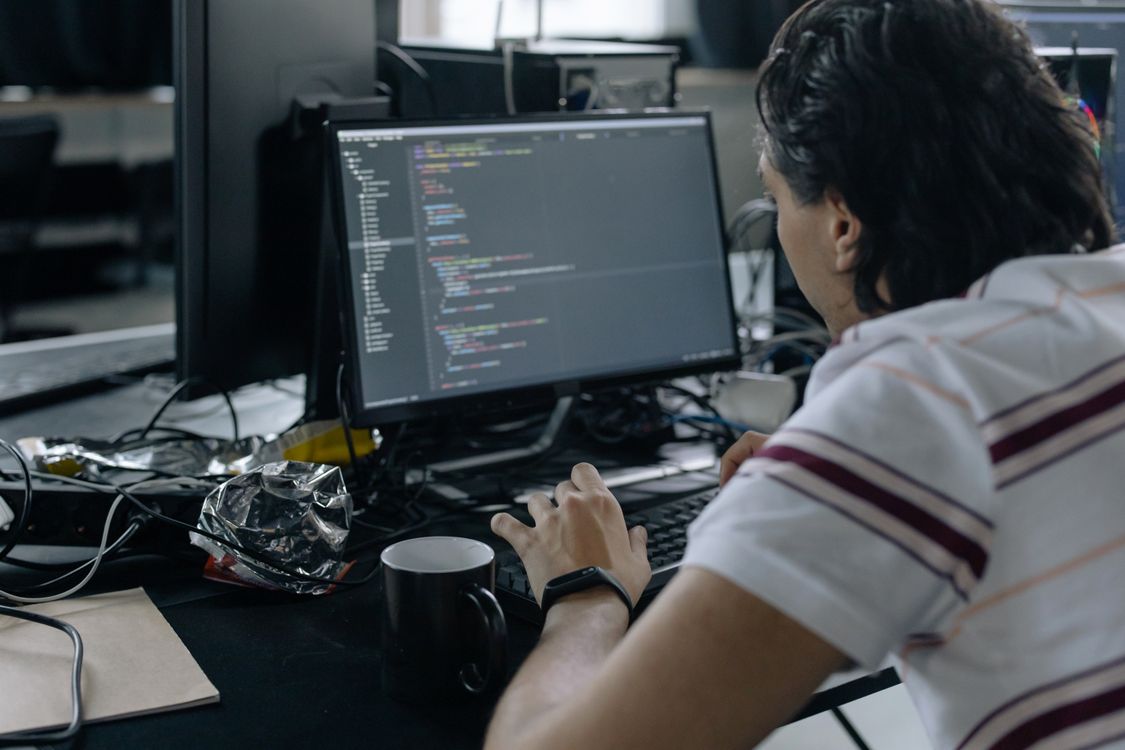 Person typing on black keyboard with black monitor displaying code on glass desk