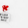 Lightbox with Black Friday Sale text and white gift box with red ribbon on white marble surface