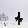 miniature metal shopping cart with blue handle and white gift box with black ribbon
