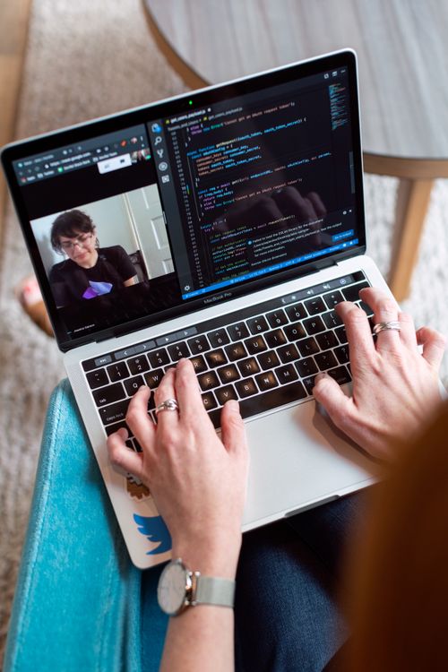 Laptop with silver metal body showing coding screen and video call, hands typing on black keyboard