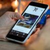 smartphone with plastic casing displaying e-commerce site held by hands with credit card
