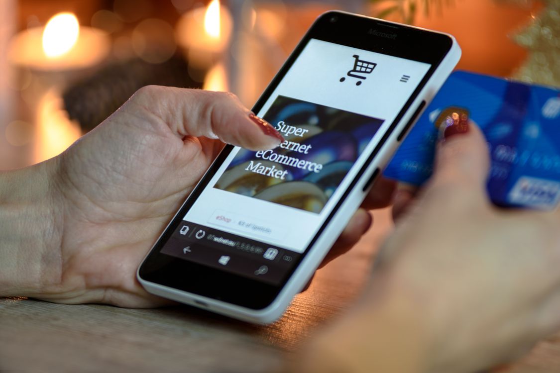 smartphone with plastic casing displaying e-commerce site held by hands with credit card