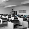 Rows of computer workstations with plastic dividers and black monitors in a white office space