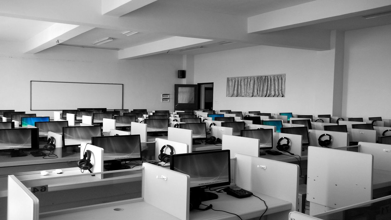 Rows of computer workstations with plastic dividers and black monitors in a white office space